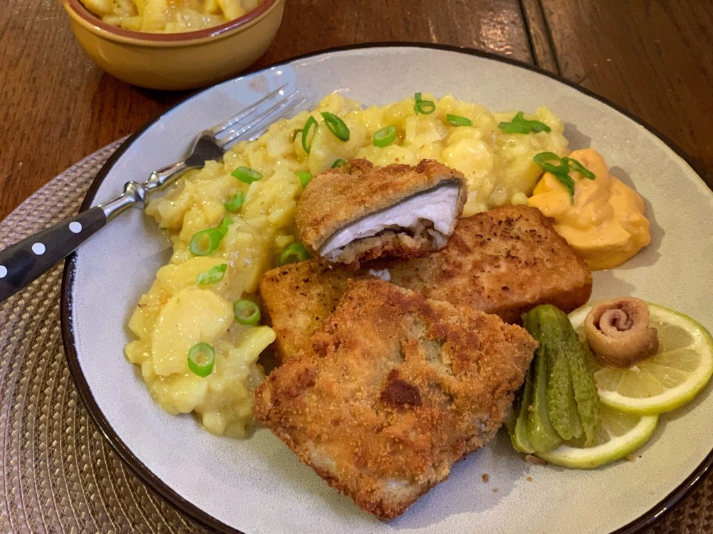 Gebackenes Zanderfilet im Schwarzwälder Schinkenmantel mit Kartoffelsalat auf einem Teller