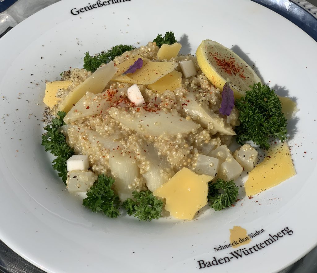 Quinoa mit Spargelstücken und Mairrübchenstücken in einem flachen Teller. Garniert mit Petersilie.