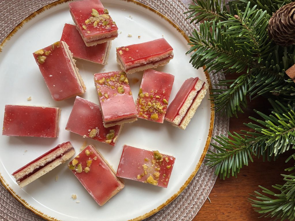 Johannisbeeren-Schnitten auf einem weißen Teller. Neben dem Teller ist ein Tannenzweig abgebildet.
