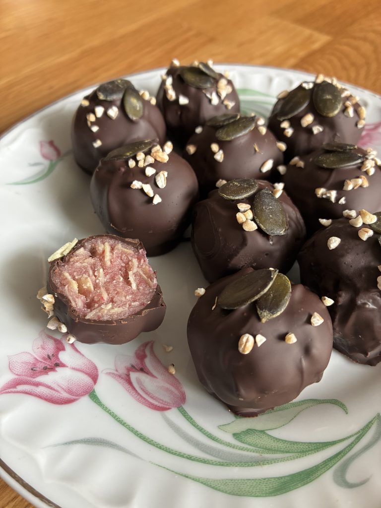Marzipankugeln, die mit Schokolade ummanterlt sind, auf einem Teller mit aufgemaltem Tulpenmuster. Die Kugeln sind mit Krokantstückchen und Kürbiskernen betreut. Eine Kugel ist angeschnitten.